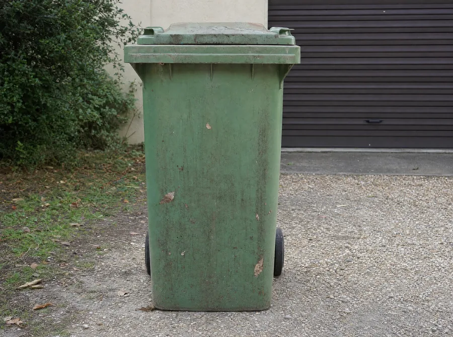 Poubelle verte sale devant un garage